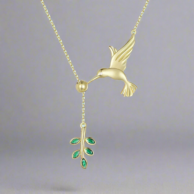 A gold necklace featuring a hummingbird and a branch with green leaf details.